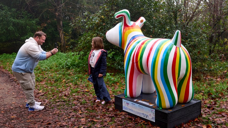 A man taking a picture of a girl in front of colourful striped sculpture of a snowdog.